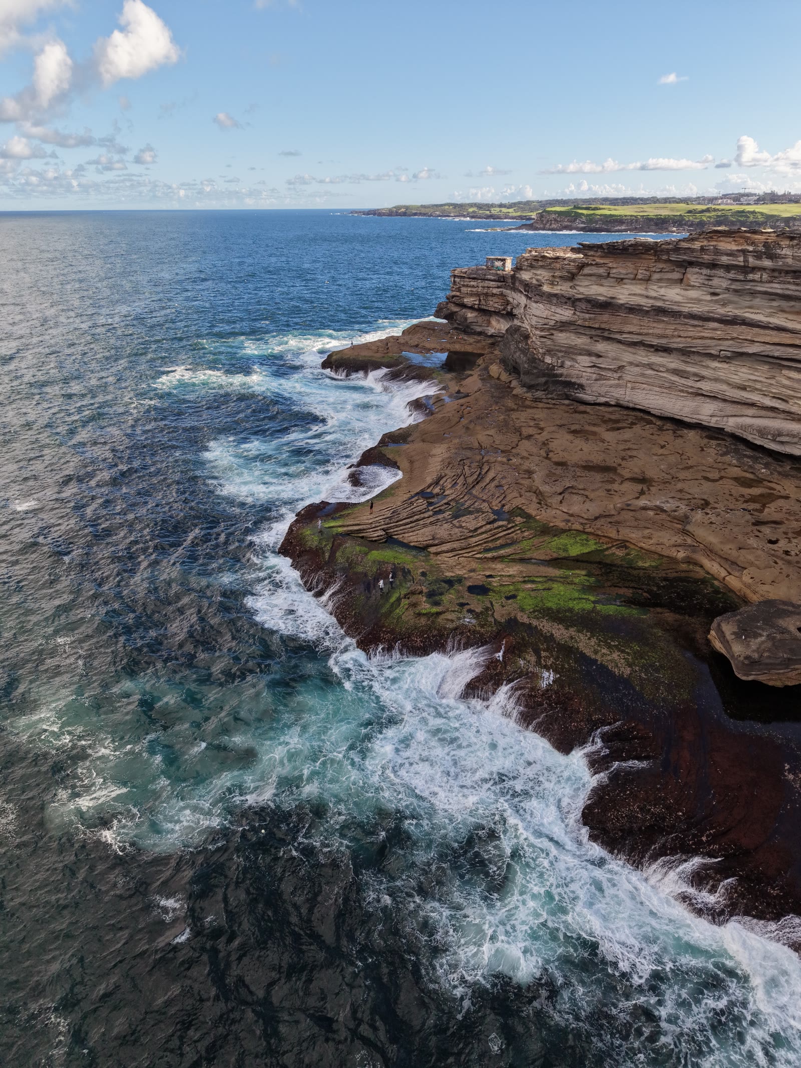 Layered sandstone headland with waves washing over the mossy rock shelf below